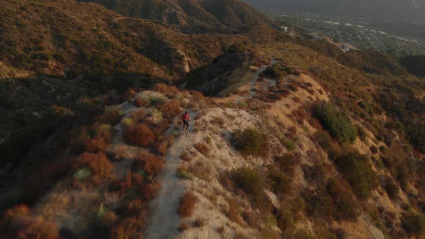 A person on a bicycle is riding down a mountain trail with mountains in the distance