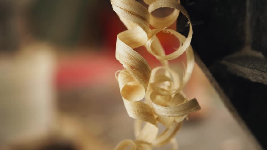 Curls of wood shavings hang off black frame as person walks in background