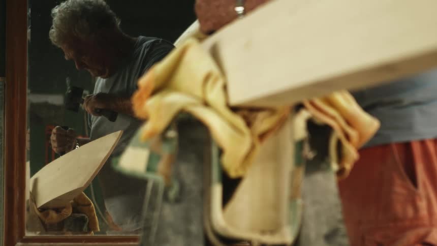 A man in a room using a mallet and a chisel on a piece of wood with a mirror in the background