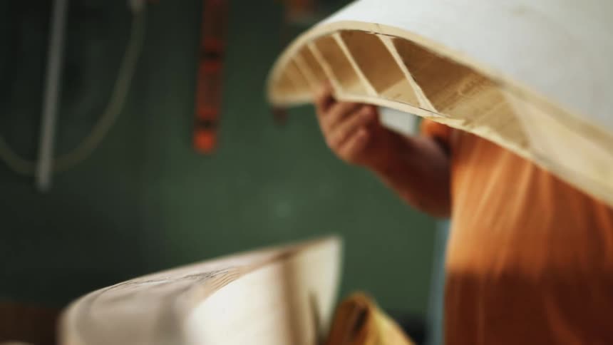 An older man is holding part of a wood crafting project while standing in a workshop