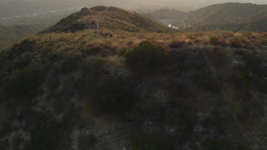 A cyclist rides along a dirt path on a mountain ridge during the day