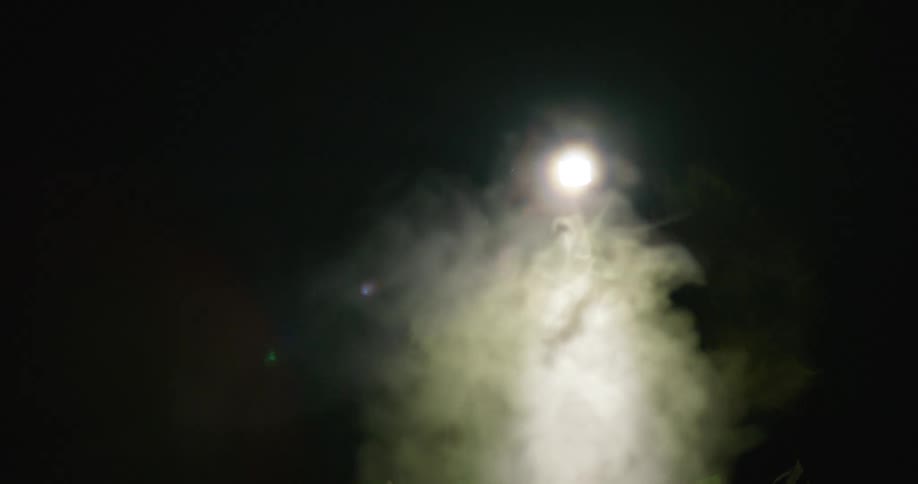 A woman wearing winter hiking gear and a headlamp is looking for something on a winter night