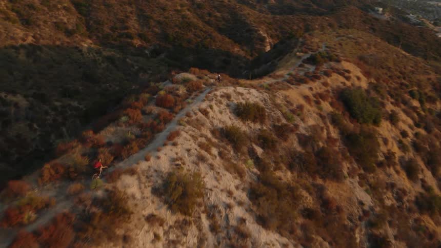 Aerial view of a cyclist running on a dirt road atop a mountain at sunset