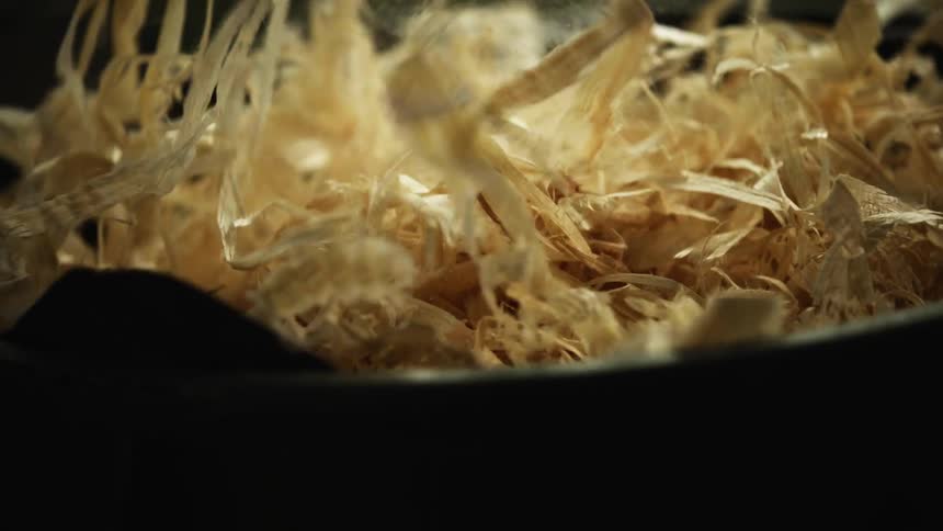 A man reaches his hand in to a container of wood shavings and picks up a handful