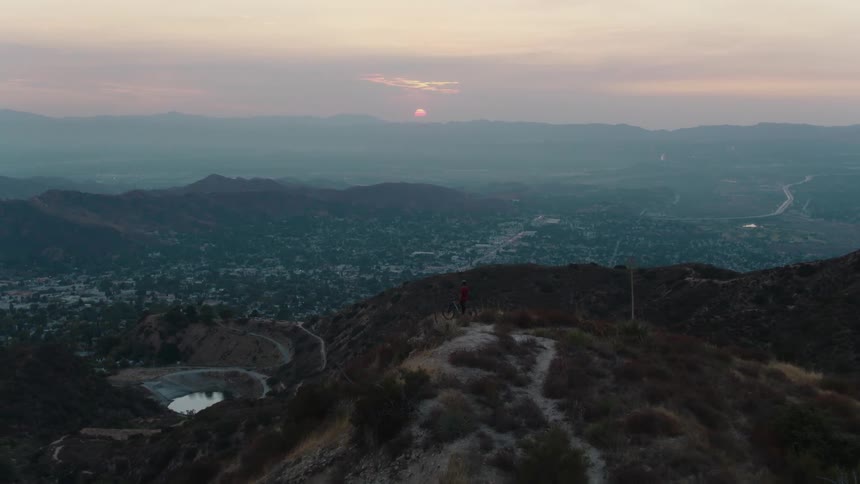 Aerial view of a cyclist standing on a lookout over town at sunset