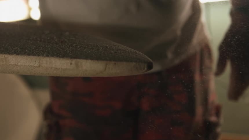 Man wipes dust off unpainted freshly sanded surfboard