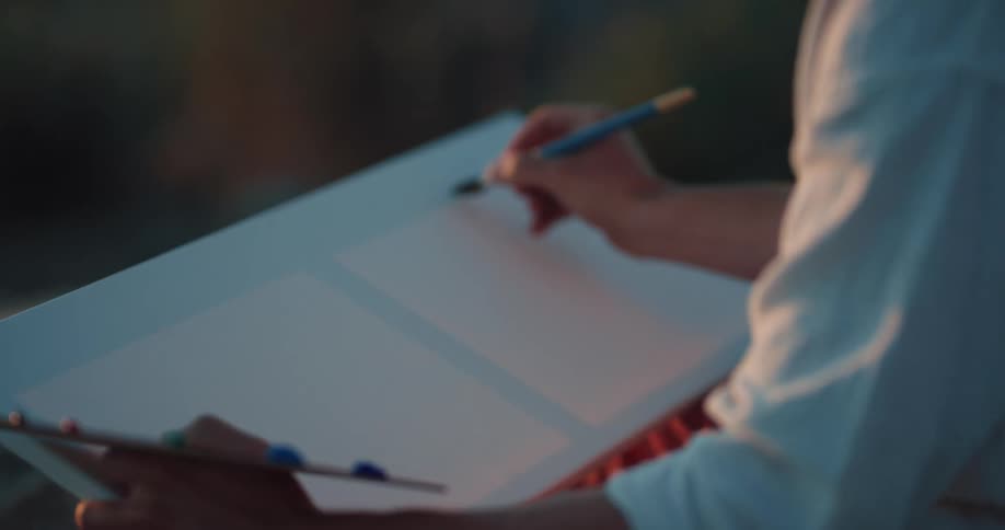 A man is sitting outdoors and painting on a canvas