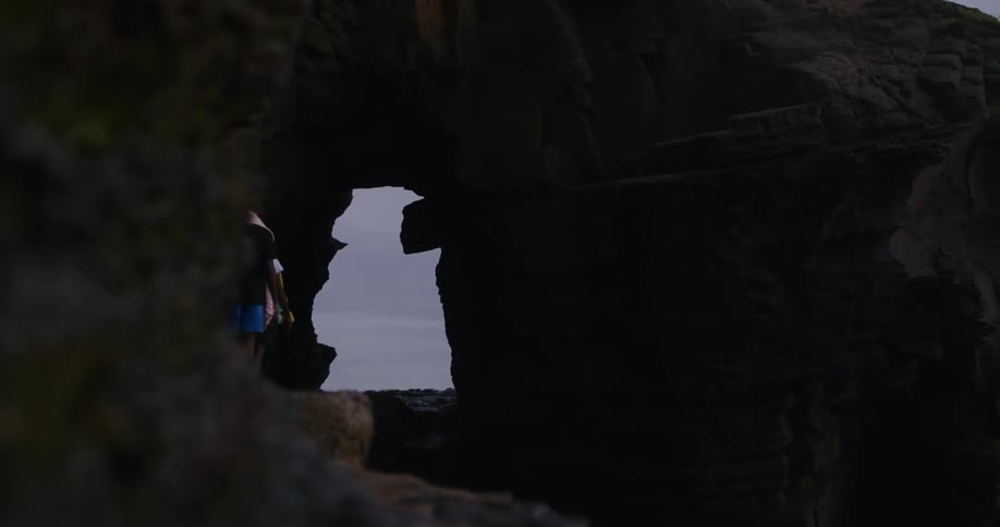 Two boys walk on a narrow path through a rock formation to the opening at the ocean