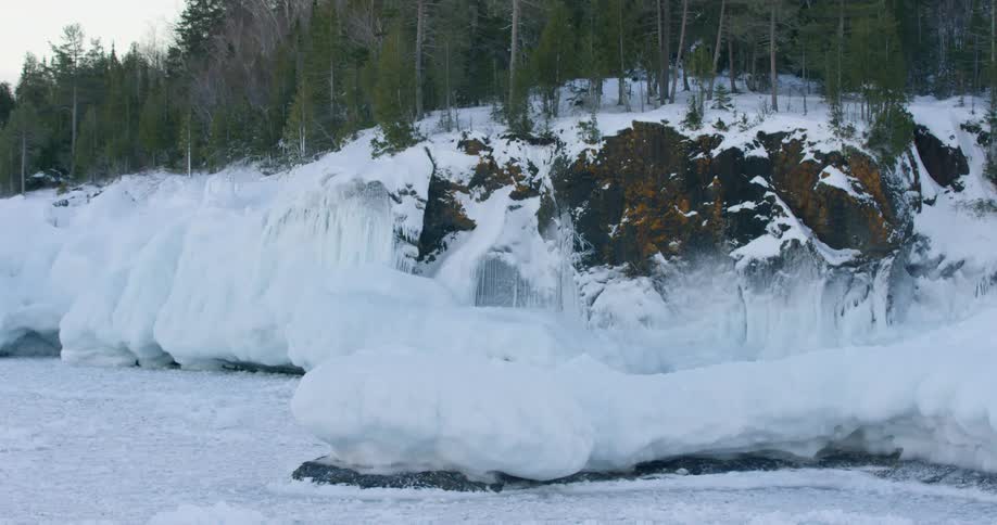 Snow covers ground as conifer forest sits on edge of sharp fall off near frozen water
