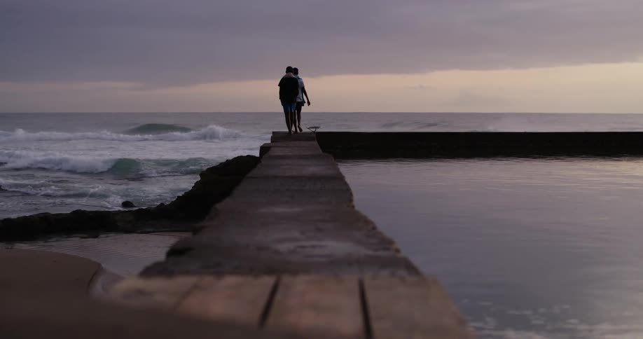 Two people are walking on a dock at dusk
