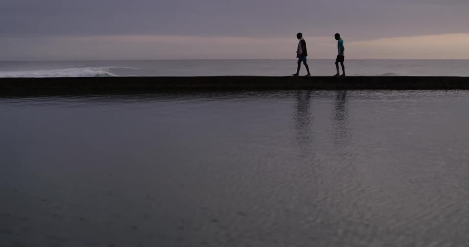 Silhouette of two people walking on a sand bank next to the ocean at sunset