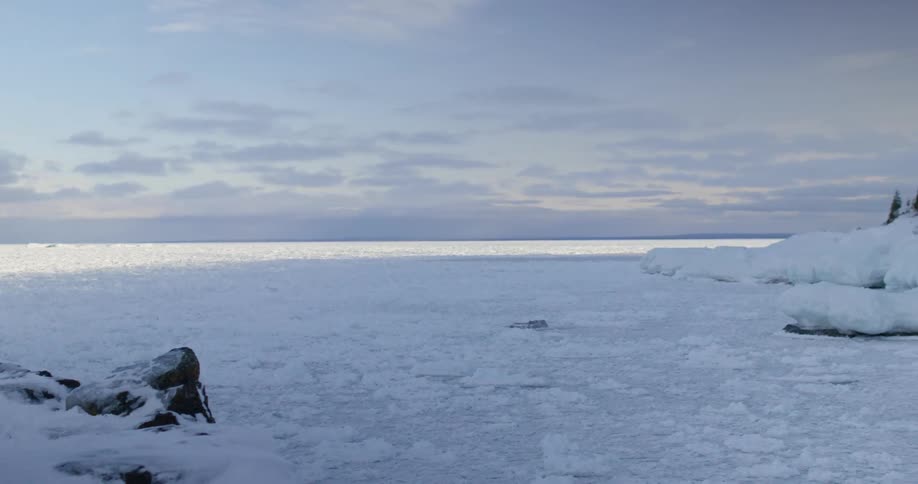 Ice covered lake and snow covered shoreline under a cloudy sky