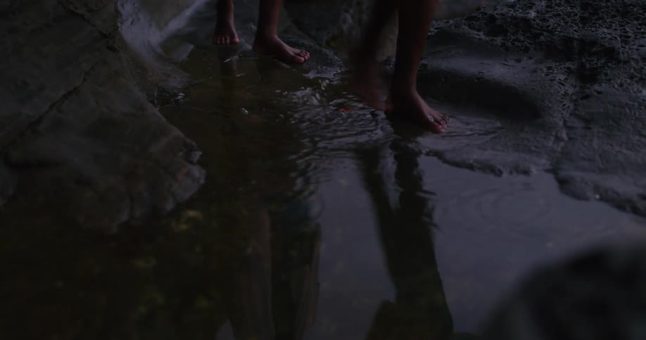 A reflection of two boys as they walk on the shore and then walk through a puddle of water