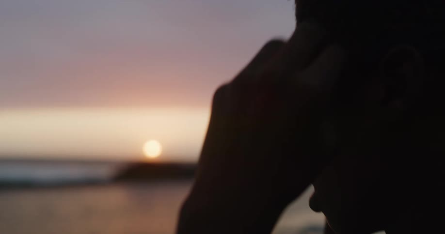 A boy putting on goggles on a beach with the sunset the sky and clouds in the background