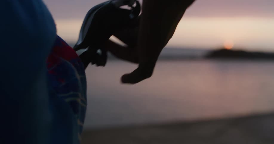 Sun hovers on horizon as two people stand on beach and one removes swim goggles from a pocket