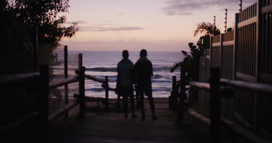 Two people are standing on a dock by the water at dusk