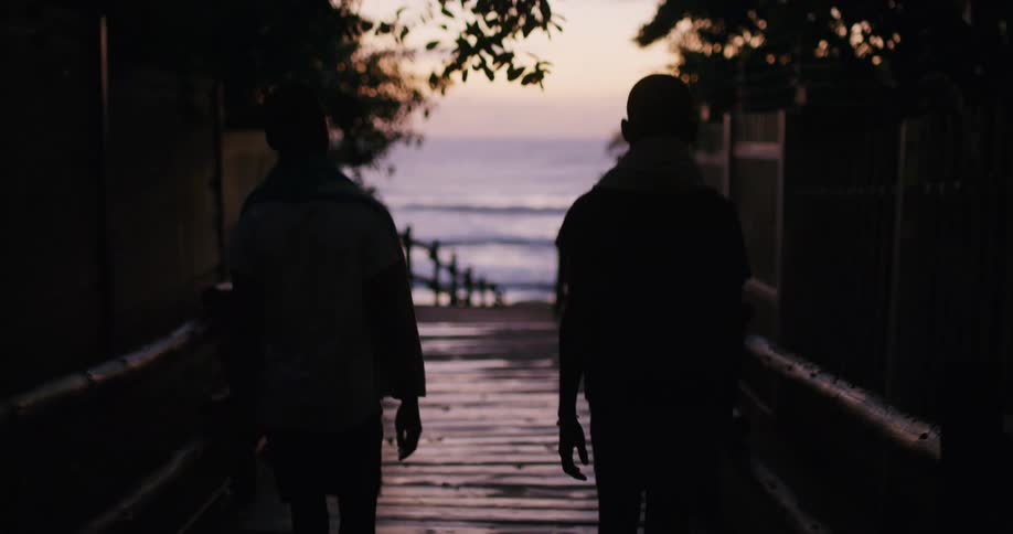 Two boys with towels over their shoulders walk down the pier towards the water