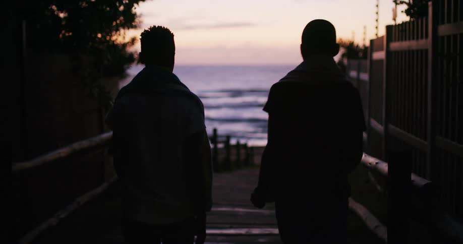 A silhouette of two people walking towards the beach with the ocean sky and clouds in the background