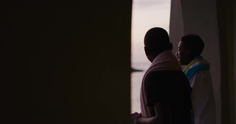 Two teenage boys stand by window with towels around their shoulders discussing swim strokes