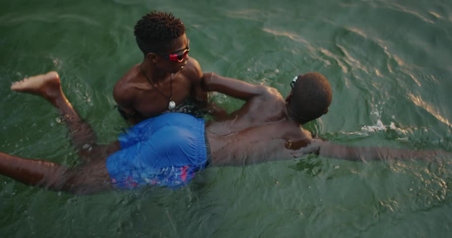 A teenager supports his brothers body as he learns to swim in a pool