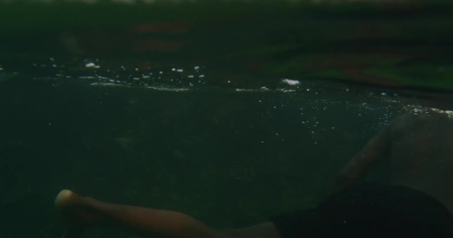 A young man is swimming underwater among the rocks while shirtless during the day