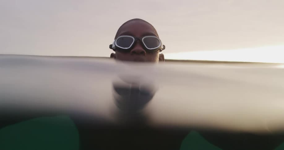 Teenager wearign swimming goggles floating in the ocean at sunset