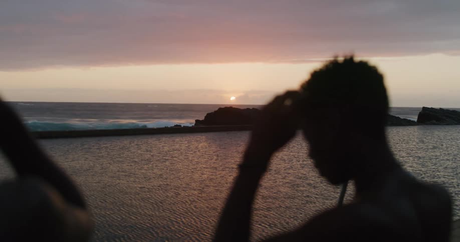 A boy near the coast putting on goggles with the sunset the ocean the sky and clouds in the background