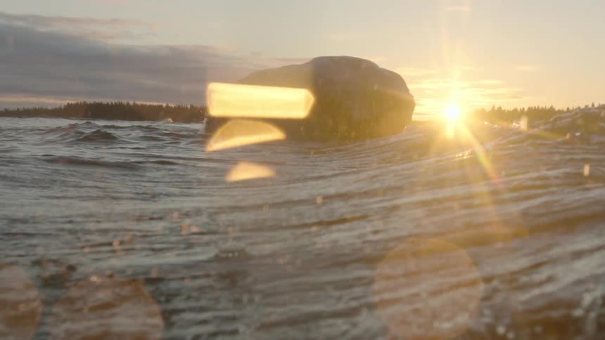 A large wave moves past a rock in the water