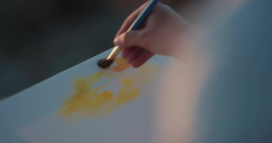 Painter painting over canvas using a palette and a brush at sunset