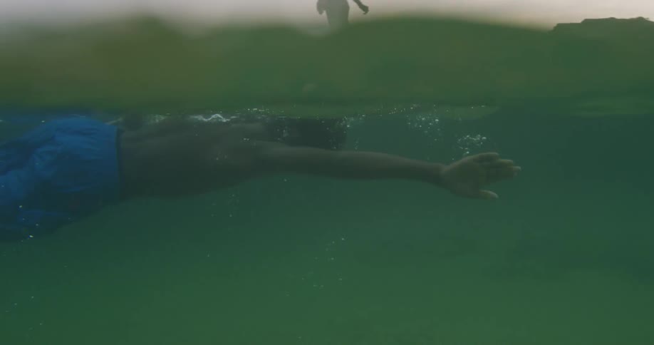 A young boy swims in a lake as another boy walks along the shore and watches him