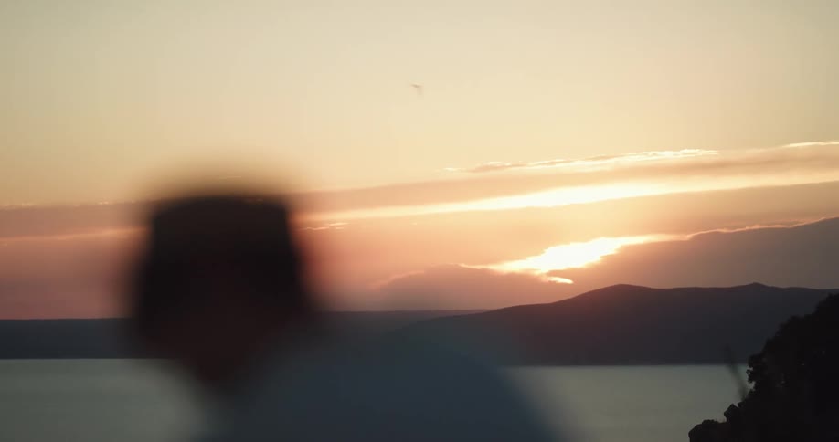 A man with a hat on looks toward the sun in the horizon