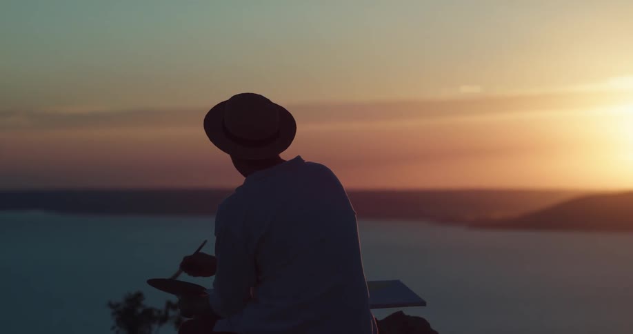An artist paints while looking out over a bay at sunset