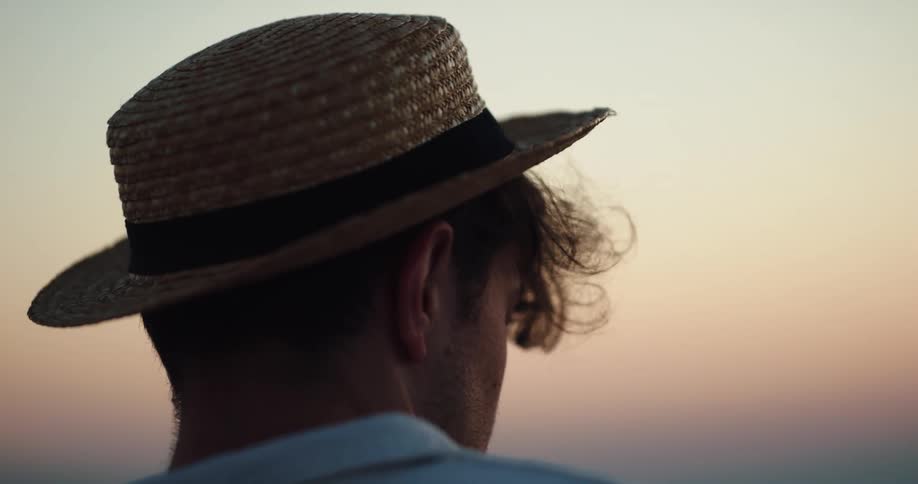A man with a shirt and hat with the sky and clouds in the background