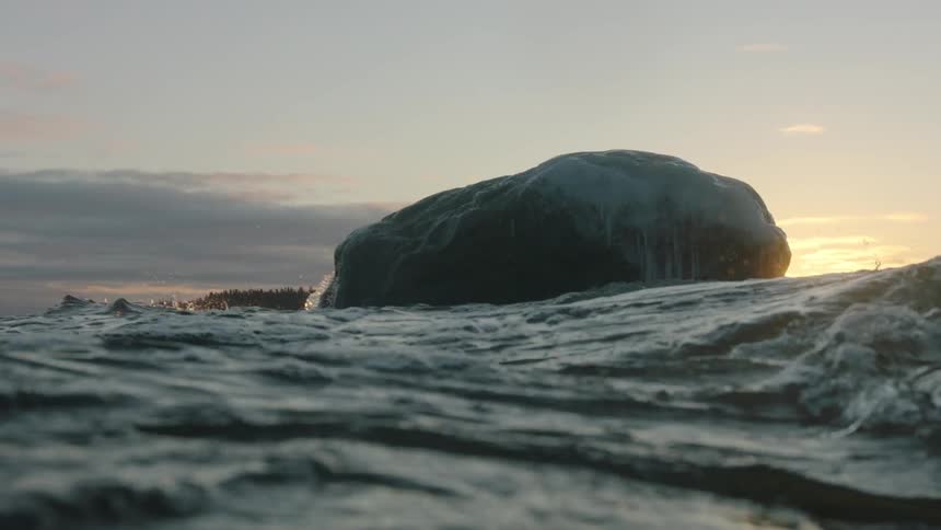 Waves surge around a large rock at sunset