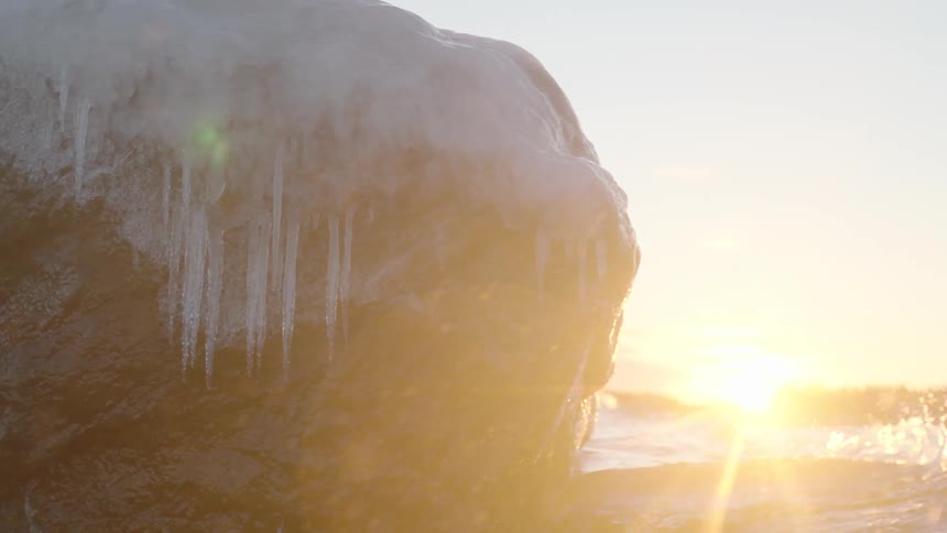 Ice hangs off a rock that is battered by waves