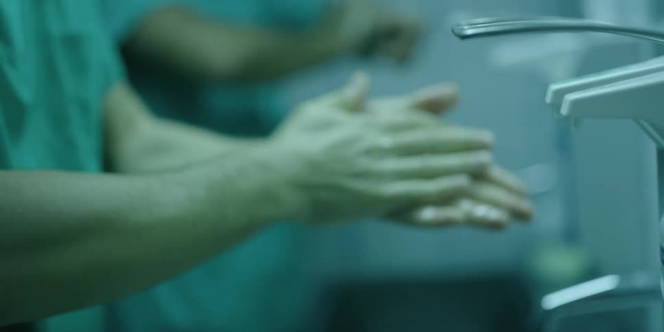 Male doctor pushes a soap dispenser with his elbow and then washes his hands with the soap