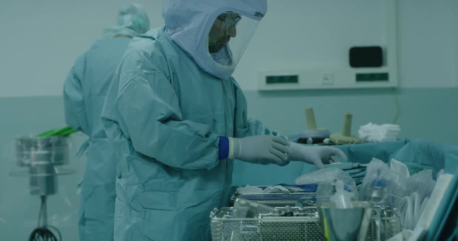 Medical personnel hand gloves to each other standing in surgical theater near medical equipment