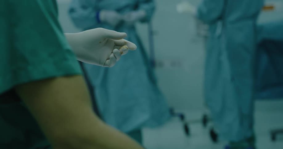 A doctor wearing scrubs is preparing for surgery while more doctors can be seen in the background