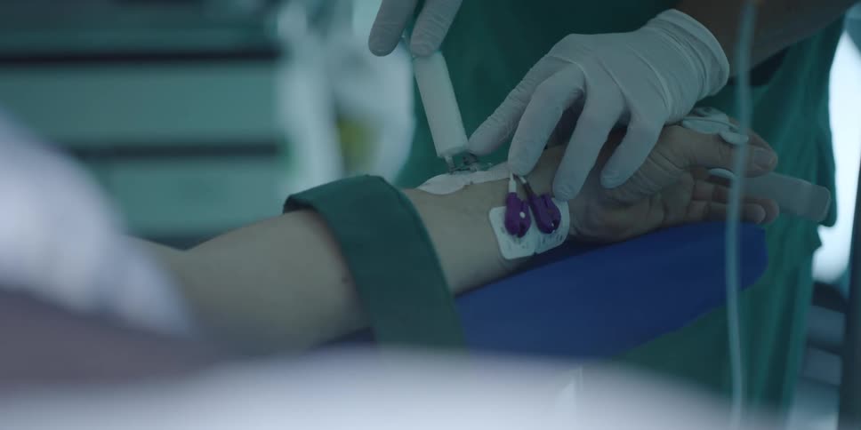Medical personnel injects medication through shunt attached to patients strapped down arm