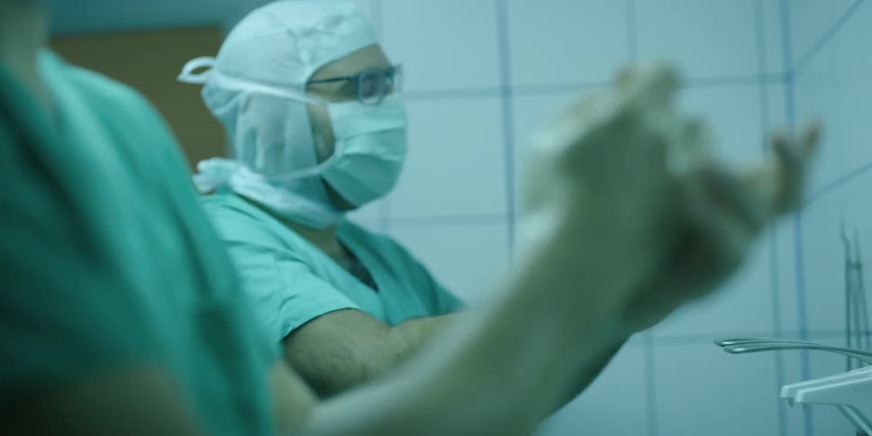 Surgical team stands in white tiled room scrubbing their hands