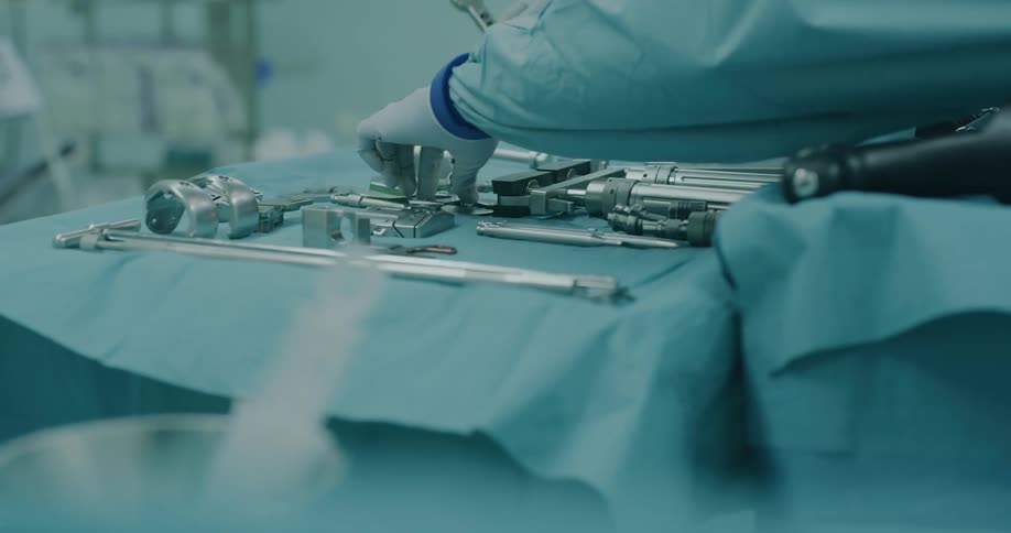 Two gloves hands pick up surgical tools from those lying on a table