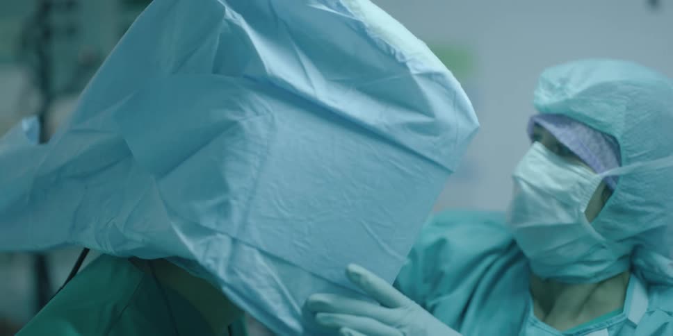 Assistants dressing a surgeon in protective gear and surgical cloth in a surgery room