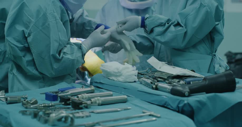 A nurse helps a doctor put gloves on in an operating room