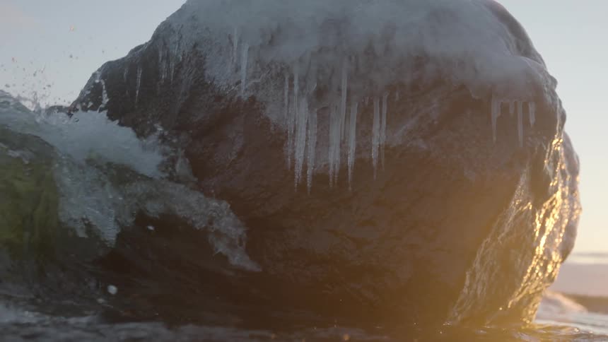 Waves crash against a large rock covered with ice