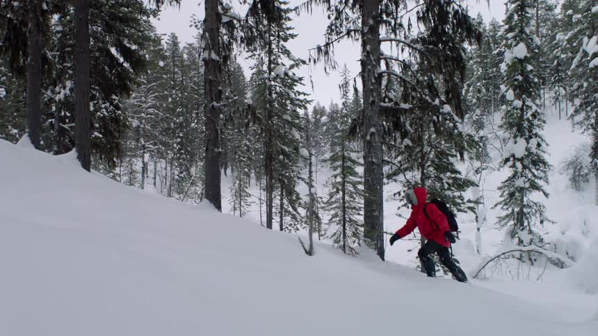 A person in a red jacket climbs up a snow hill