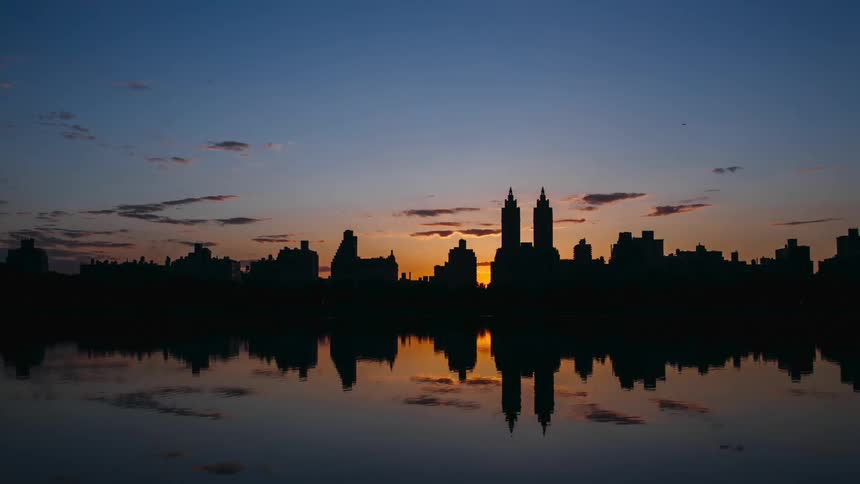 A body of water with a city skyline with buildings and skyscrapers with the sky and clouds in the background