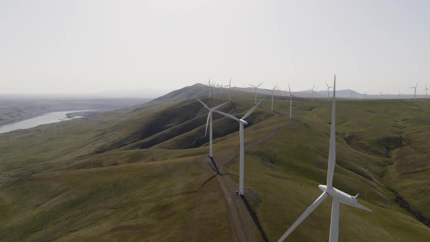 Pullback descent behind several wind turbines spinning on a hillside wind farm