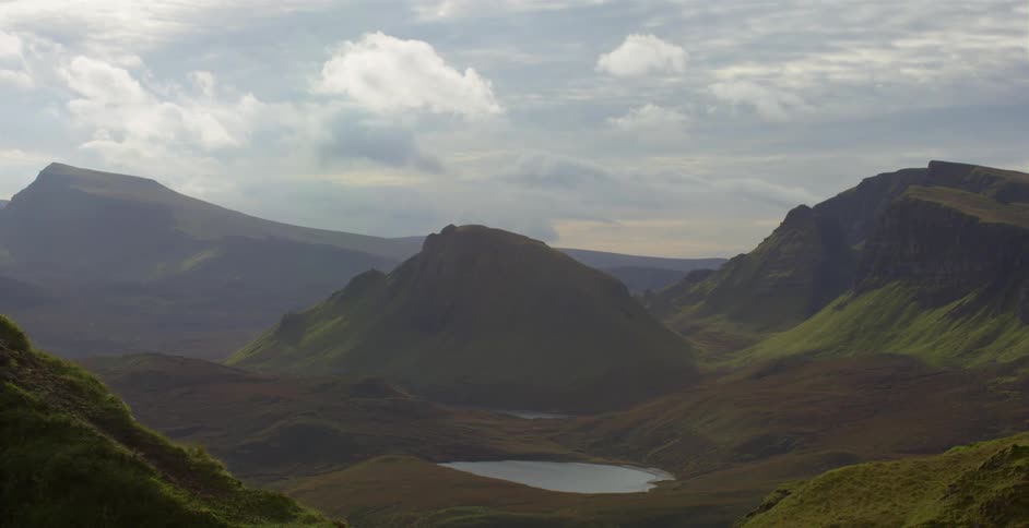 Grass covered mountains surrounding a small lake under a cloudy sky