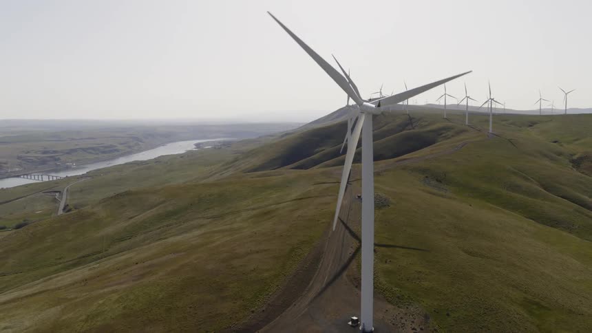Orbit around multiple wind turbines operating along the slope of green rolling hills