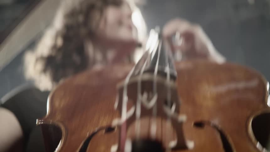 A man plays a cello under a bright light indoors